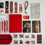 Collection of stationery items including a red notebook, pens, and decorative elements on a white background.