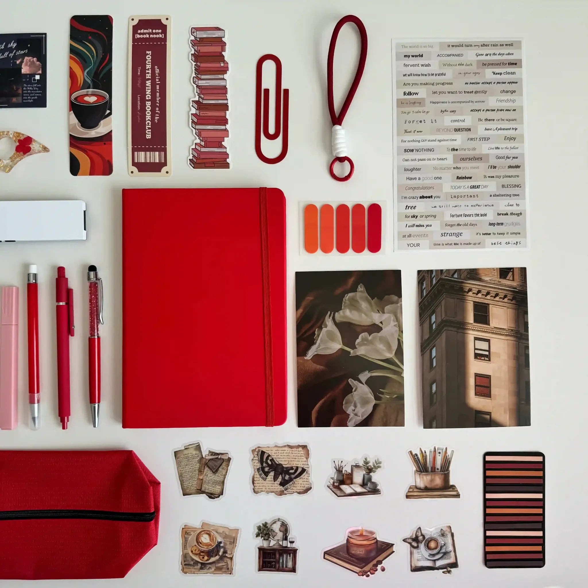 Collection of stationery items including a red notebook, pens, and decorative elements on a white background.