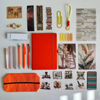Collection of stationery items including an orange notebook, pens, and clips on a white surface.