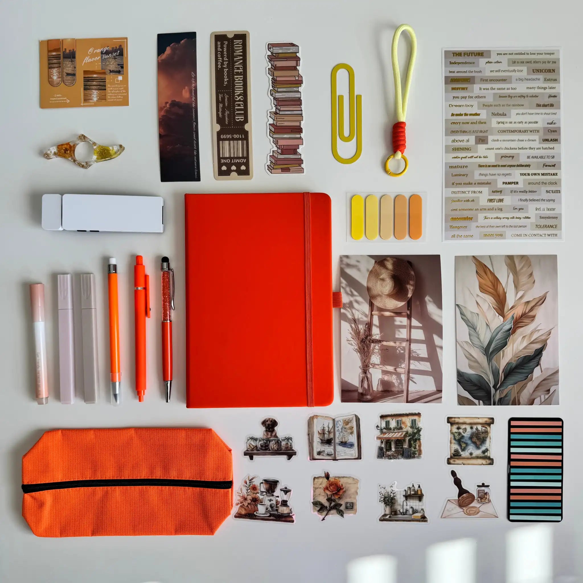 Collection of stationery items including an orange notebook, pens, and clips on a white surface.