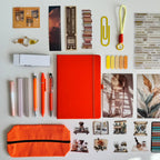 Collection of stationery items including a red notebook, pens, and photo frames on a light gray background.
