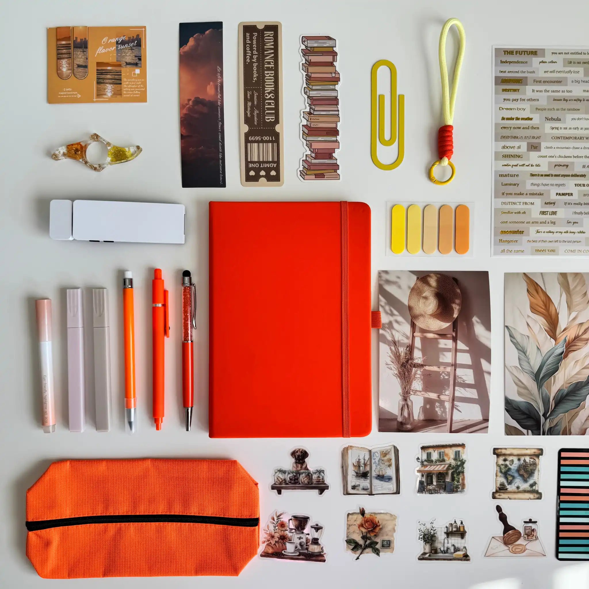 Collection of stationery items including a red notebook, pens, and photo frames on a light gray background.