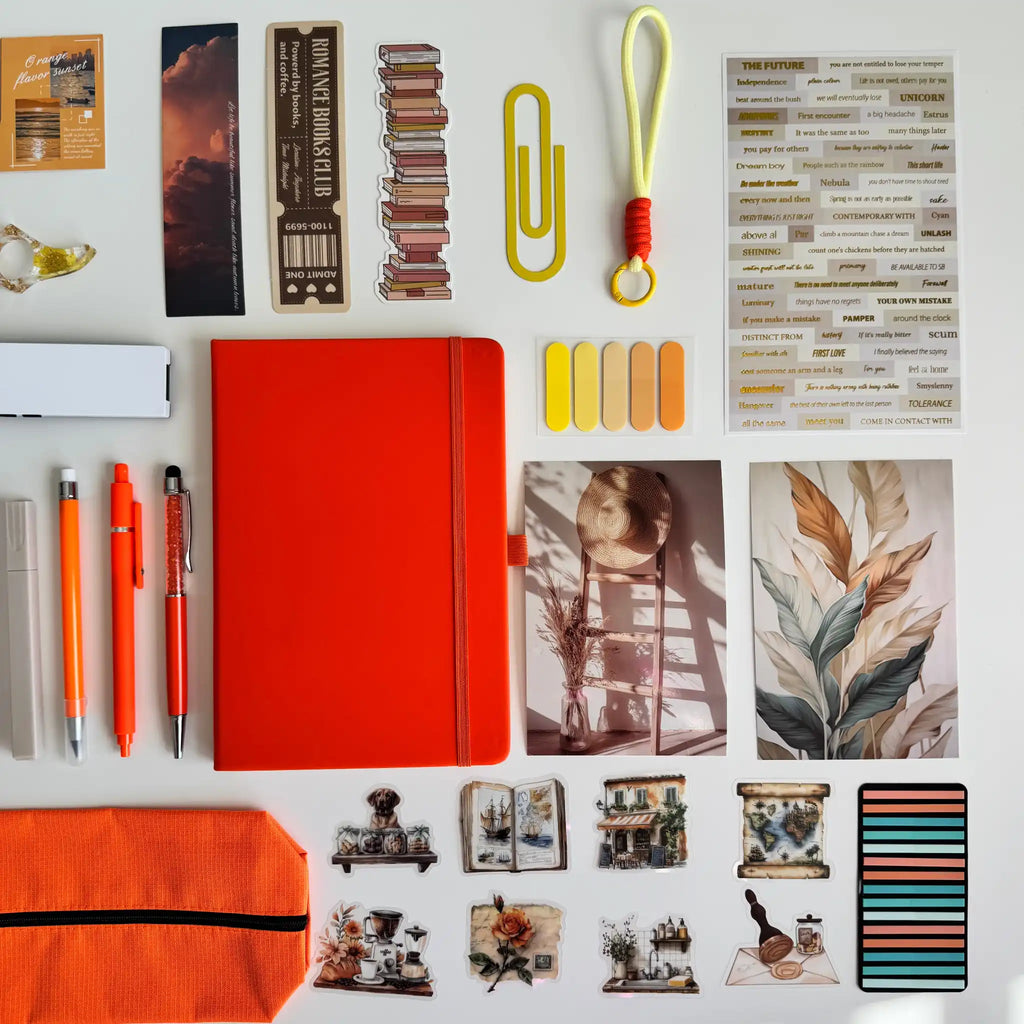 Collection of stationery items including an orange notebook, pens, and decorative elements on a white background.