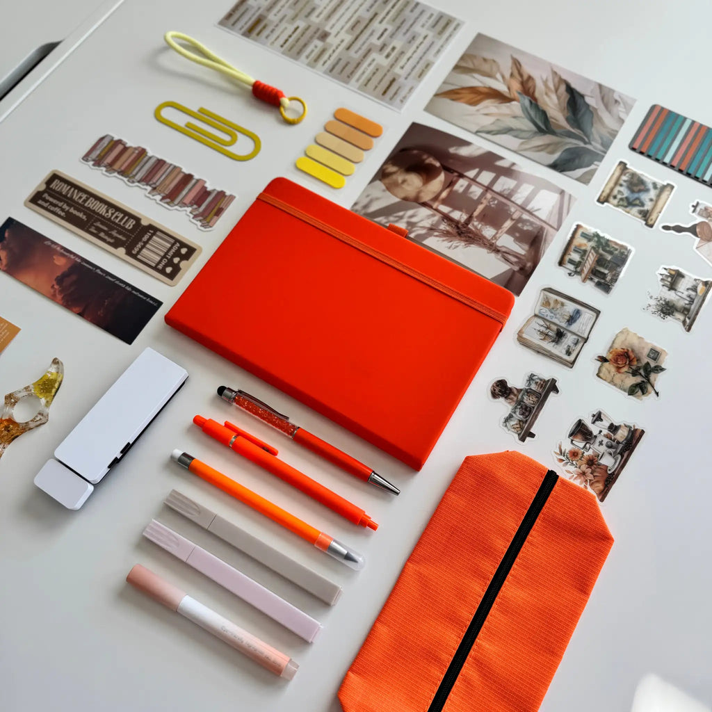 Collection of stationery items including an orange pouch, pens, and photo frames on a light surface.