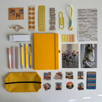 Collection of stationery items including a yellow notebook, pens, markers, and decorative elements on a white background.