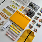 Collection of stationery items including a yellow notebook, pens, and decorative elements on a light surface.