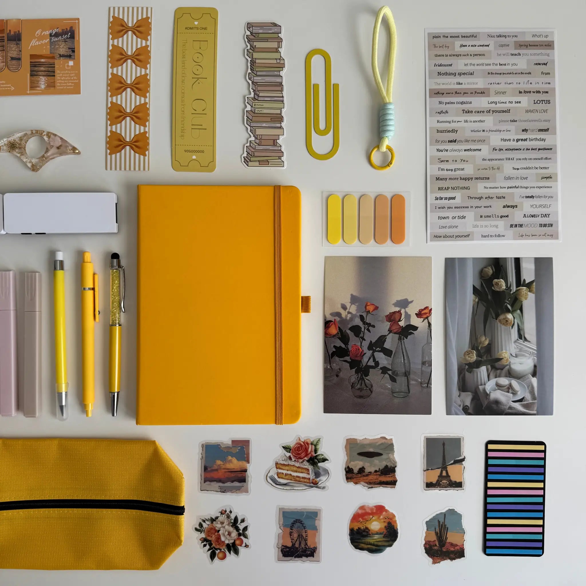 Collection of stationery items including a yellow notebook, pens, and decorative elements on a white background.