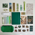 Collection of stationery items including a green notebook, pens, markers, and stickers on a white background.