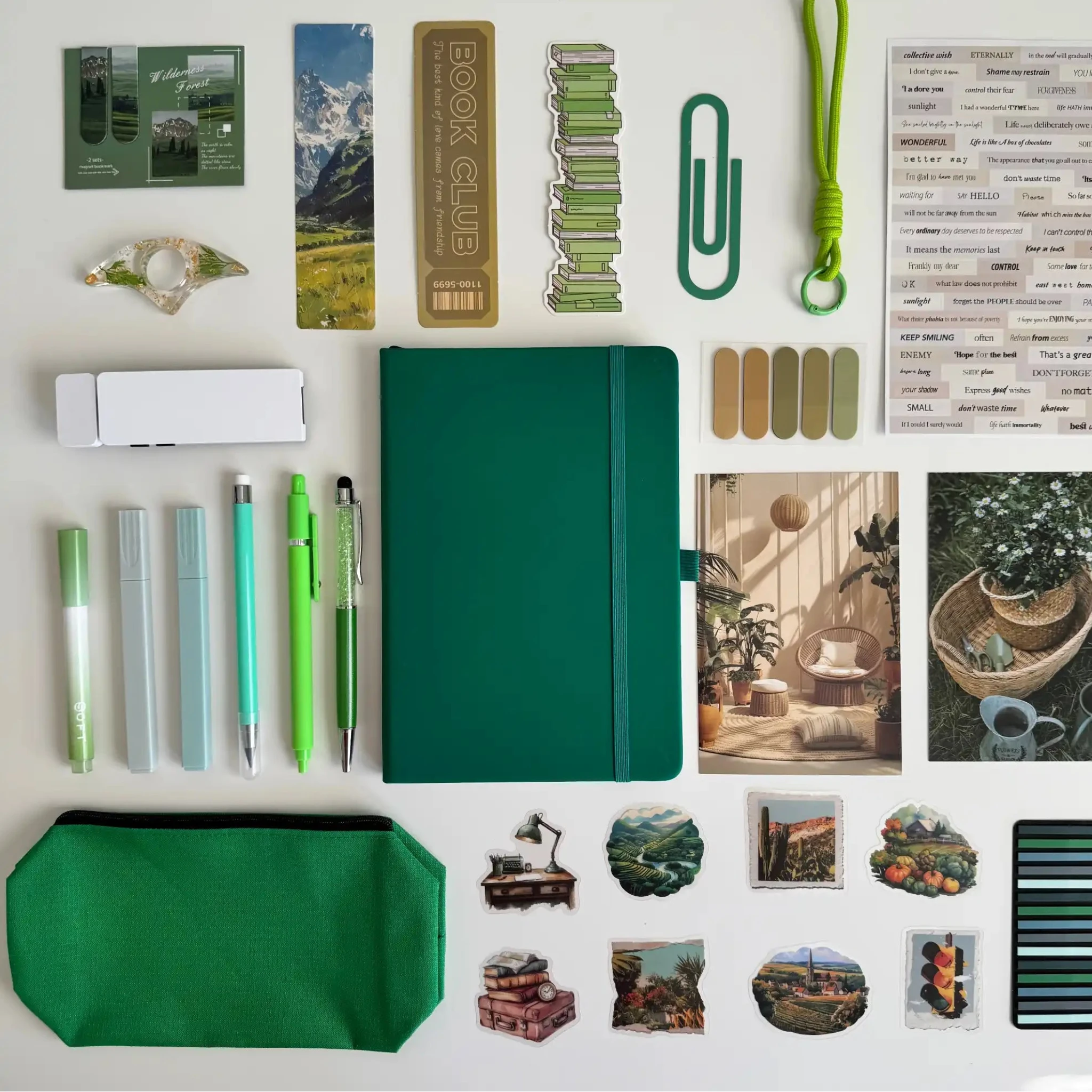 Collection of stationery items including a green notebook, pens, bookmarks, and decorative elements on a white background.