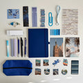 Collection of stationery items including a blue notebook, pens, markers, and photo prints on a light background