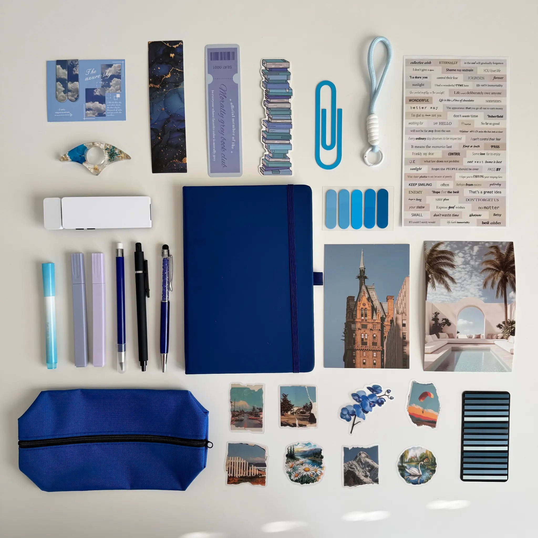 Collection of stationery items including a blue notebook, pens, markers, and photo prints on a light background