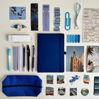 Collection of stationery items including a blue notebook, pens, markers, and photo prints on a light background.