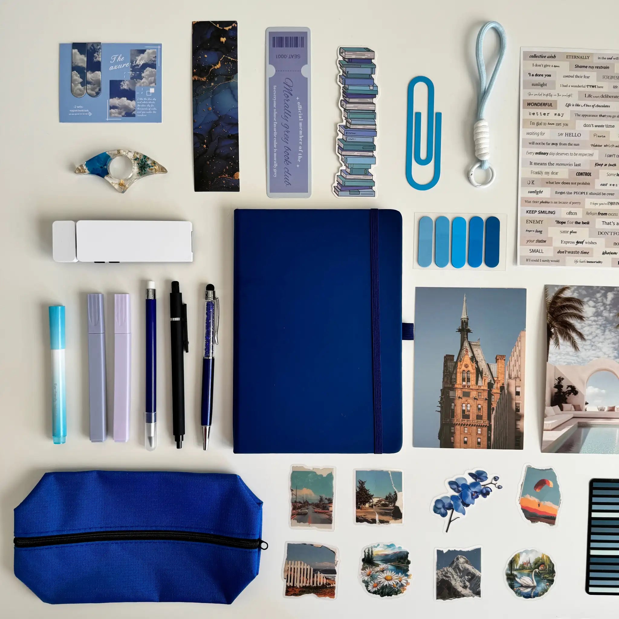 Collection of stationery items including a blue notebook, pens, markers, and photo prints on a light background.
