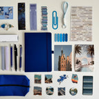Collection of stationery items including a blue notebook, pens, and photo frames on a white background