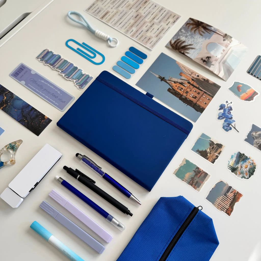 Collection of stationery items including pens, a blue notebook, and photo prints on a white surface.