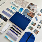 Collection of stationery items including pens, a blue notebook, and photo prints on a white surface.