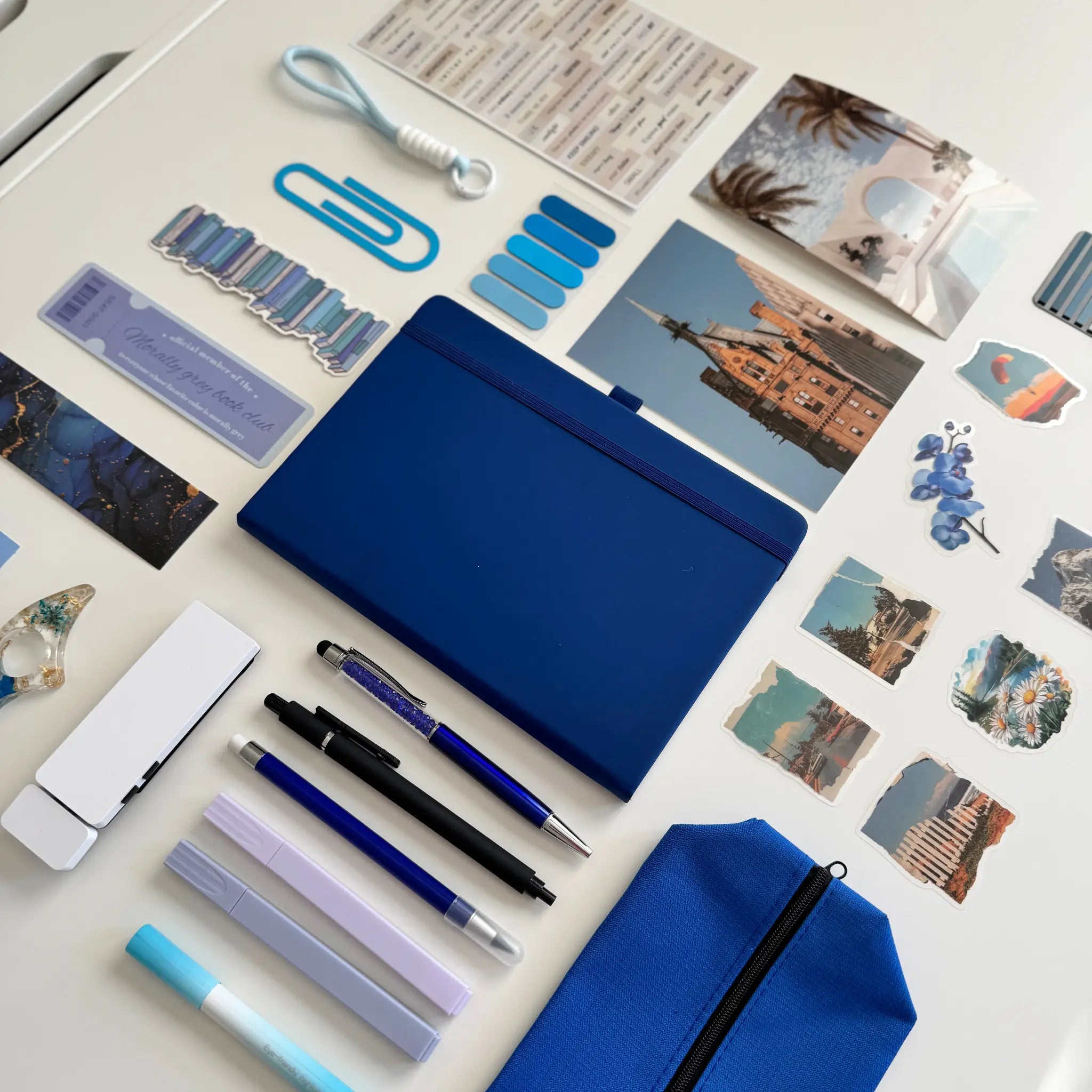 Collection of stationery items including pens, a blue notebook, and photo prints on a white surface.