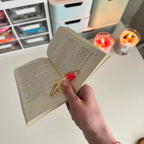 Hand holding an open book with a decorative book holder, candles in the background