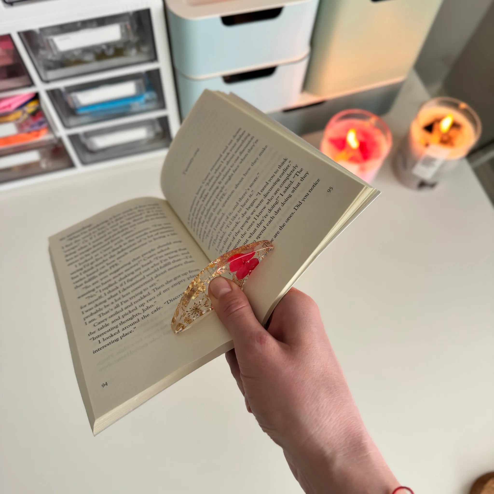 Hand holding an open book with a decorative book holder, candles in the background