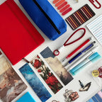 Collection of stationery items including a  notebook, pens, markers, and photo prints in blue and red colors on a light background