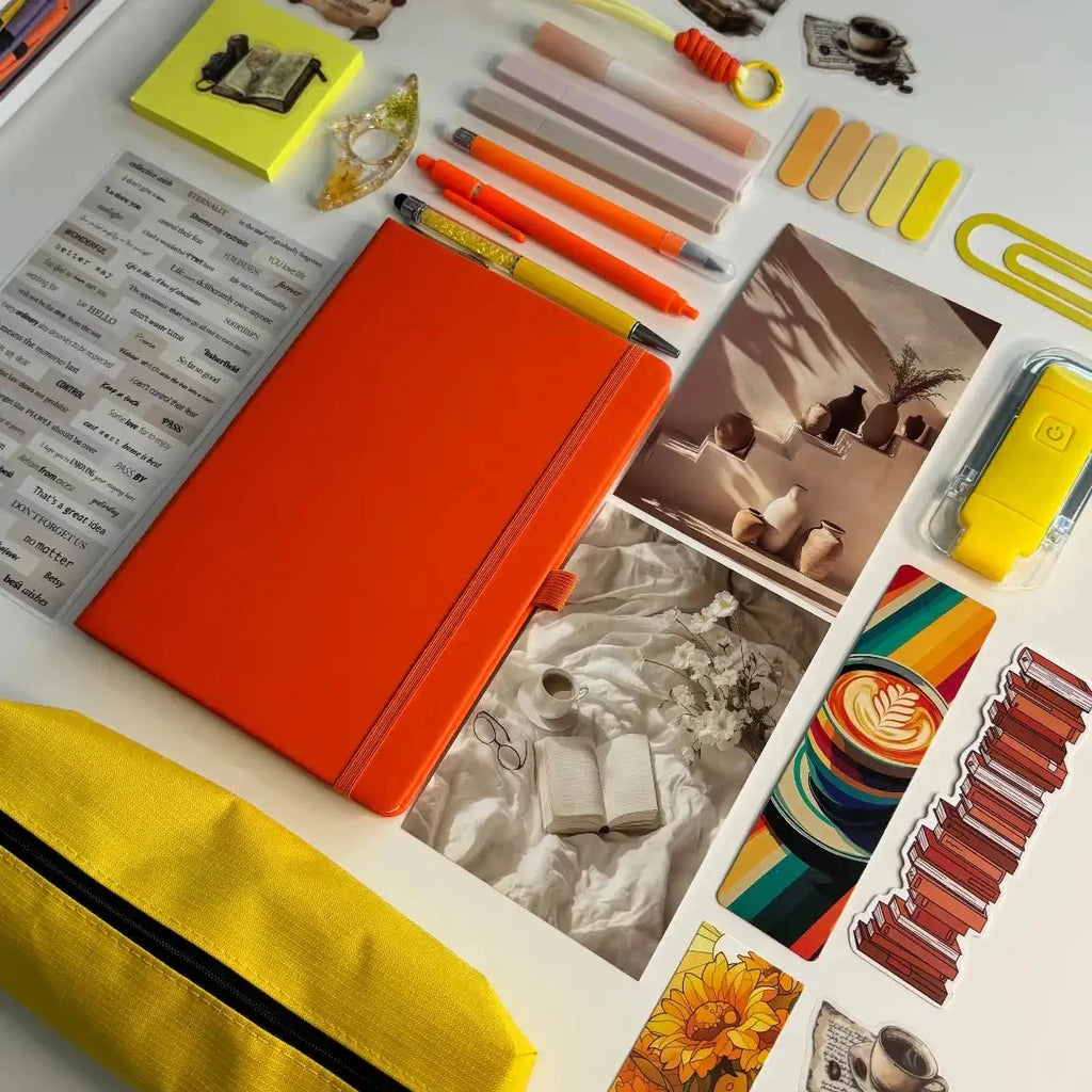 Collection of stationery items including a  notebook, pens, markers, and photo prints in orange and yellow colors on a light background