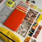 Collection of stationery items including a  notebook, pens, markers, and photo prints in orange and yellow colors on a light background