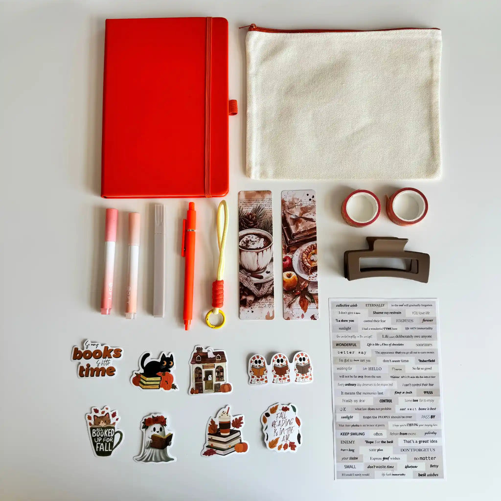 A flat-lay arrangement of stationery and desk accessories on a white background, including a red notebook, a cream fabric pouch, two lip balm tubes, a red pen, washi tapes, a hair clip, printed bookmarks, stickers, and a planner sticker sheet.