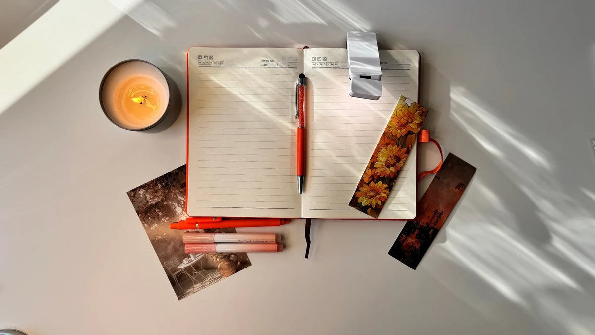 Notebook with pen, candles, and decorative items on a light surface