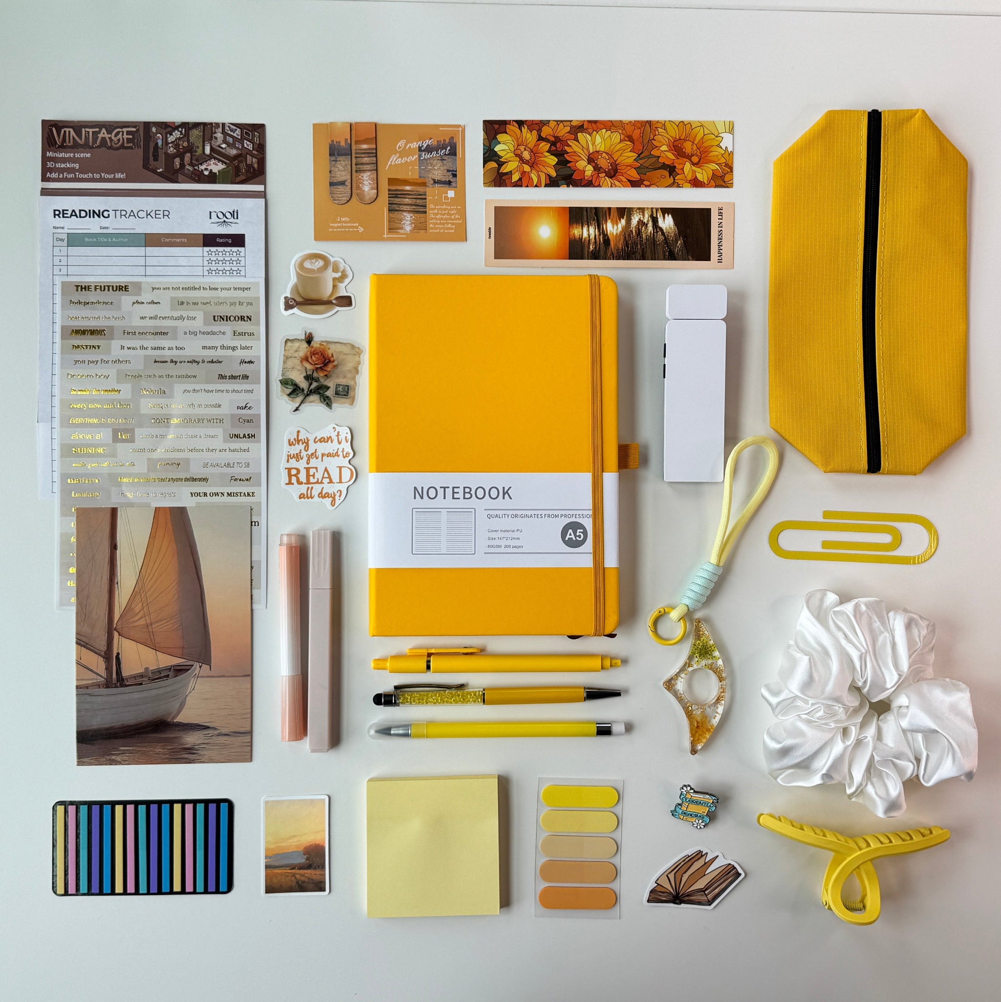 Collection of stationery items including a yellow notebook, pens, and decorative elements on a white background.