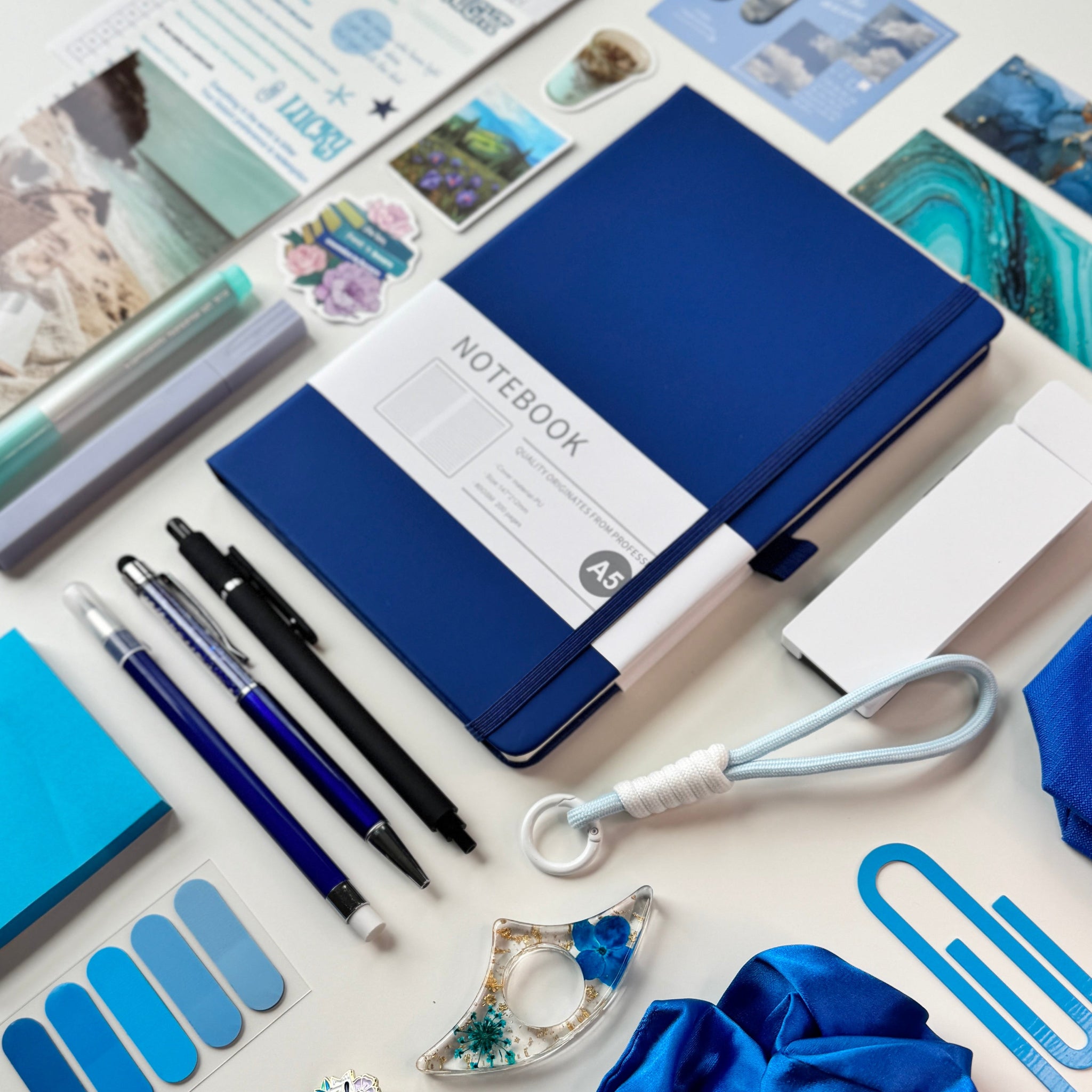 Collection of blue stationery items including a notebook, pens, and scrunchie on a white surface.