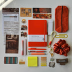 Collection of stationery items including a notebook, pens, and decorative elements on a white surface.