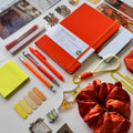 Collection of stationery items including notebooks, pens, and decorative objects on a white surface.