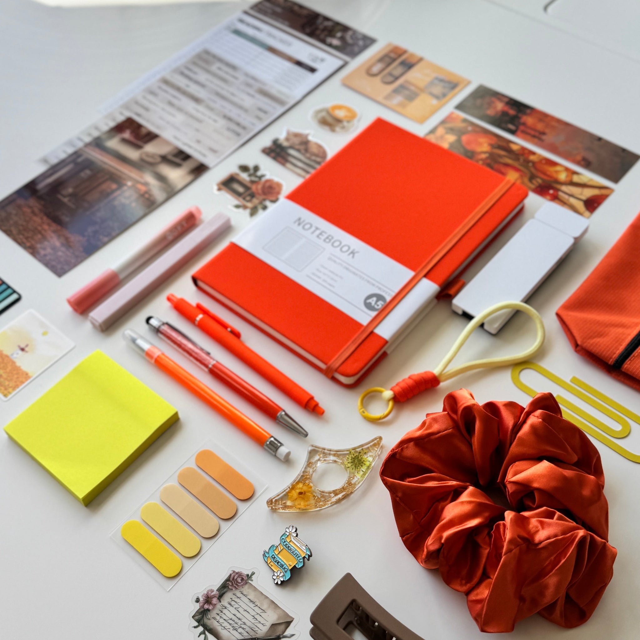 Desk with stationery items including an orange notebook, pens, sticky notes, and a scrunchie.