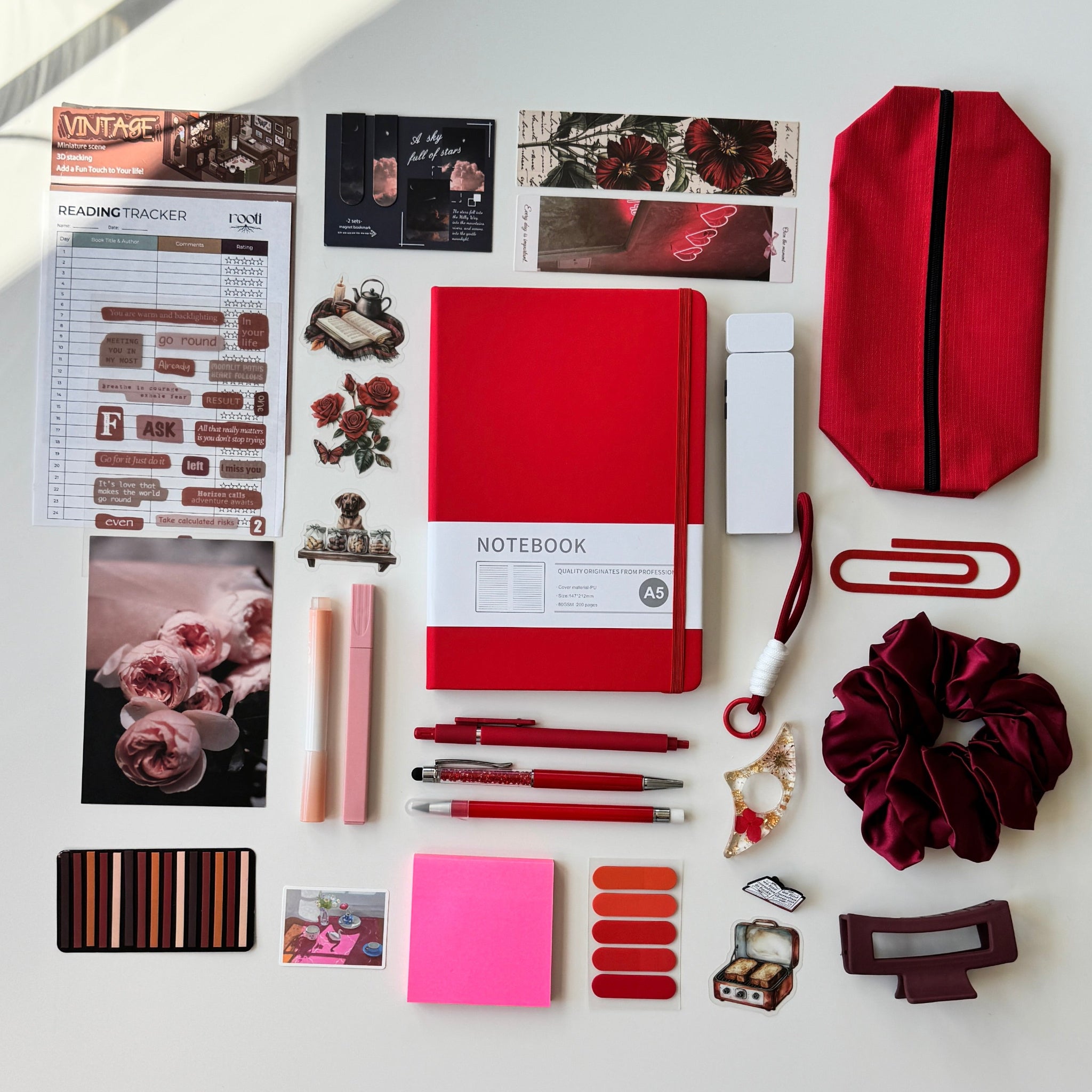 Collection of stationery items including a red notebook, pens, and clips on a white surface.