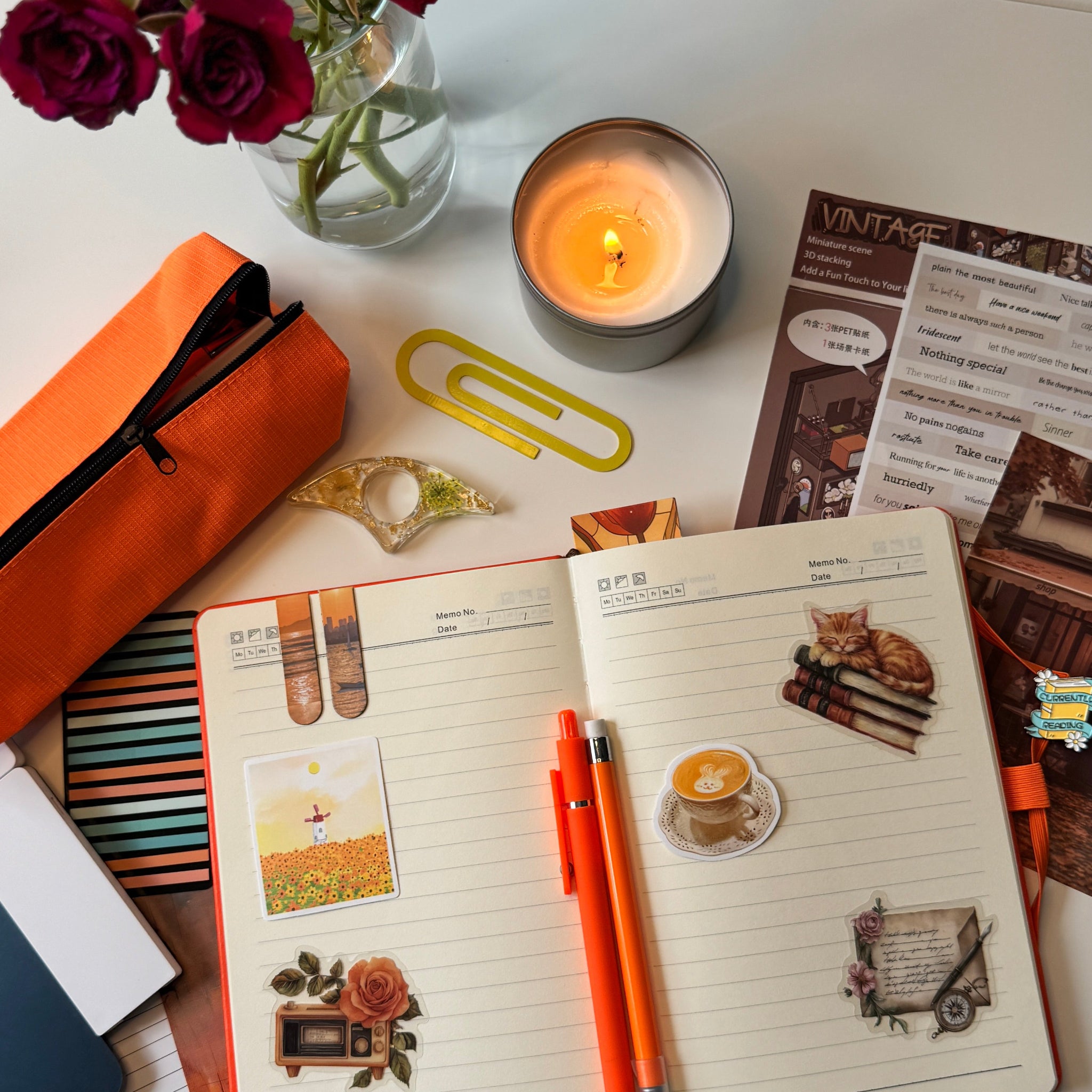 Notebook with orange pen, candle, and flowers on a desk