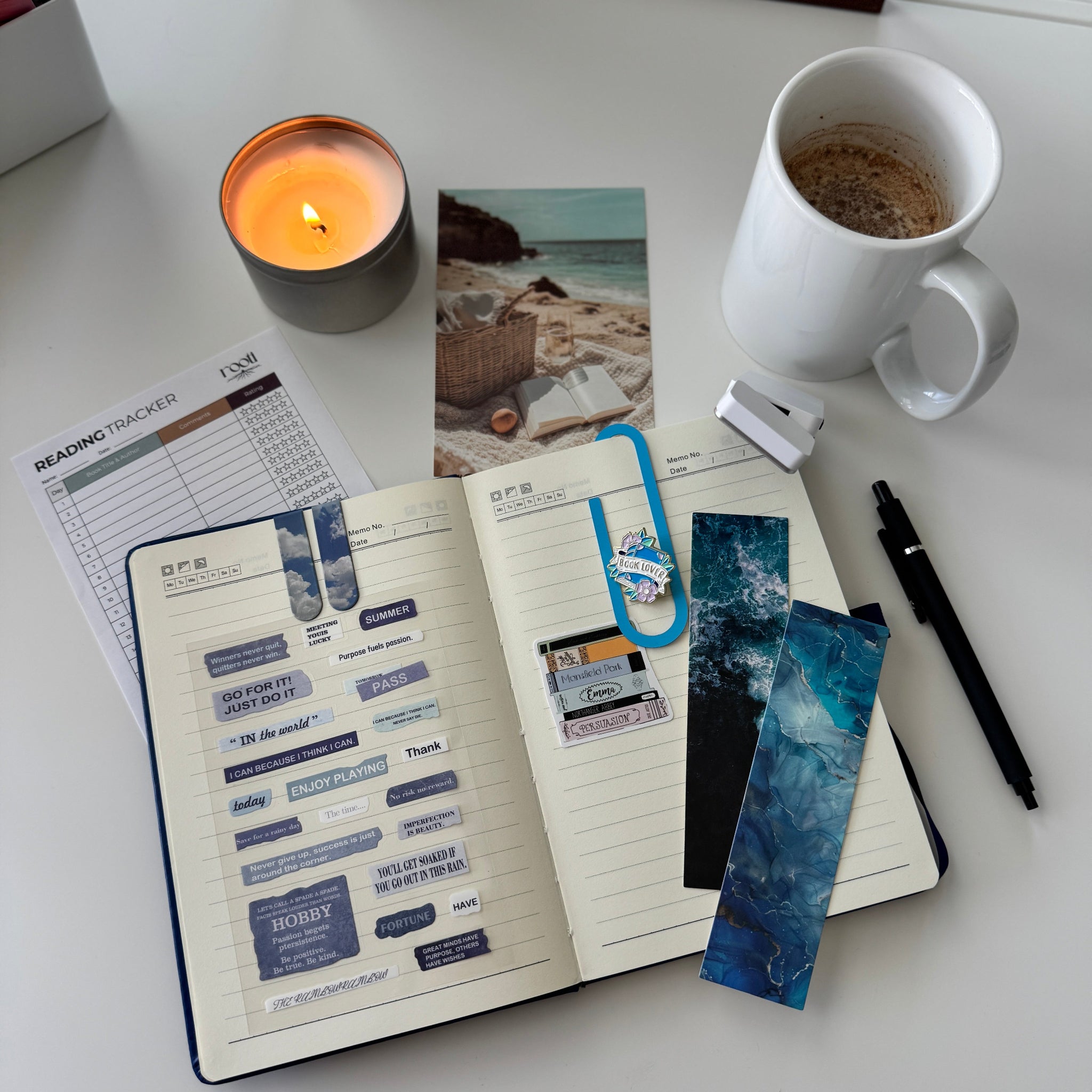 Notebook with bookmarks, a candle, a mug, and a photo on a white surface