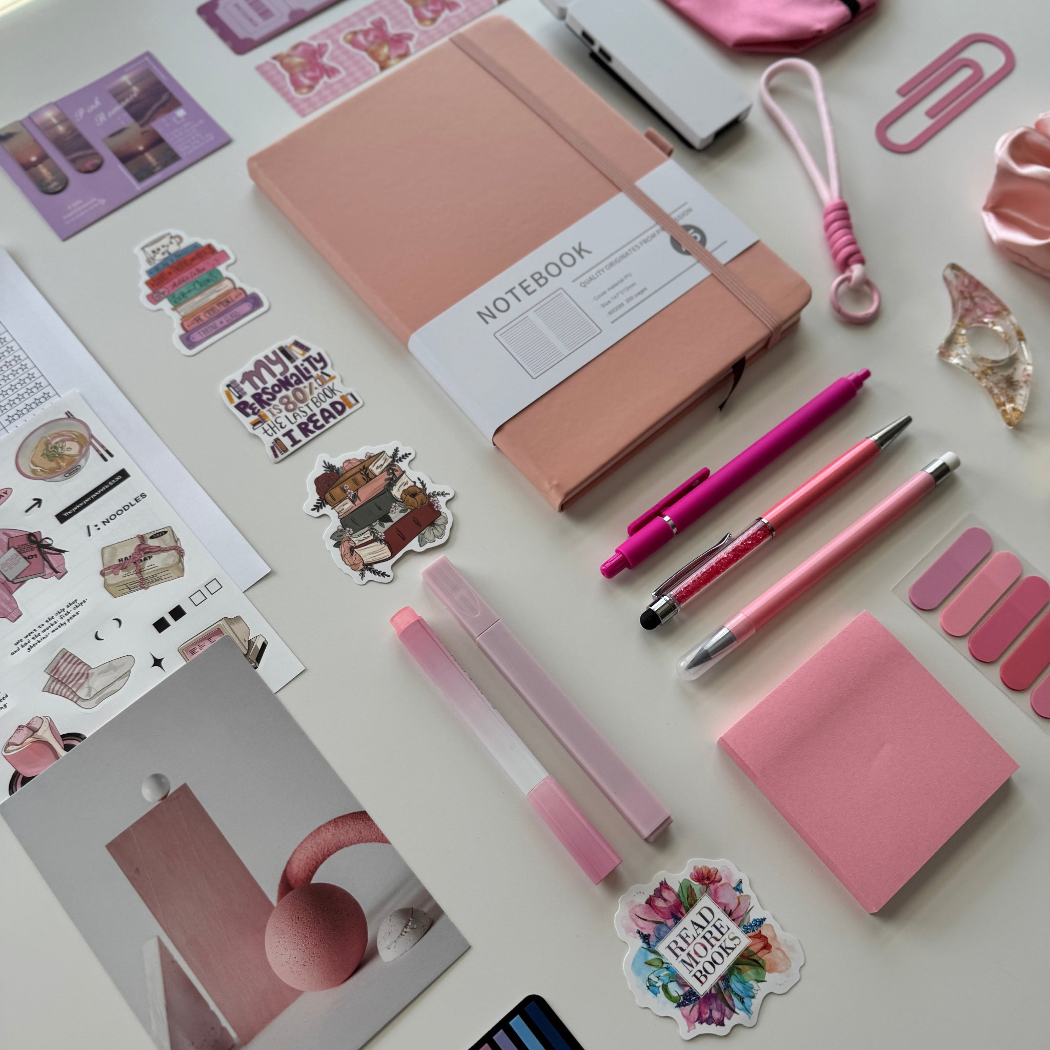 Collection of pink stationery items including a notebook, pens, and stickers on a light surface.