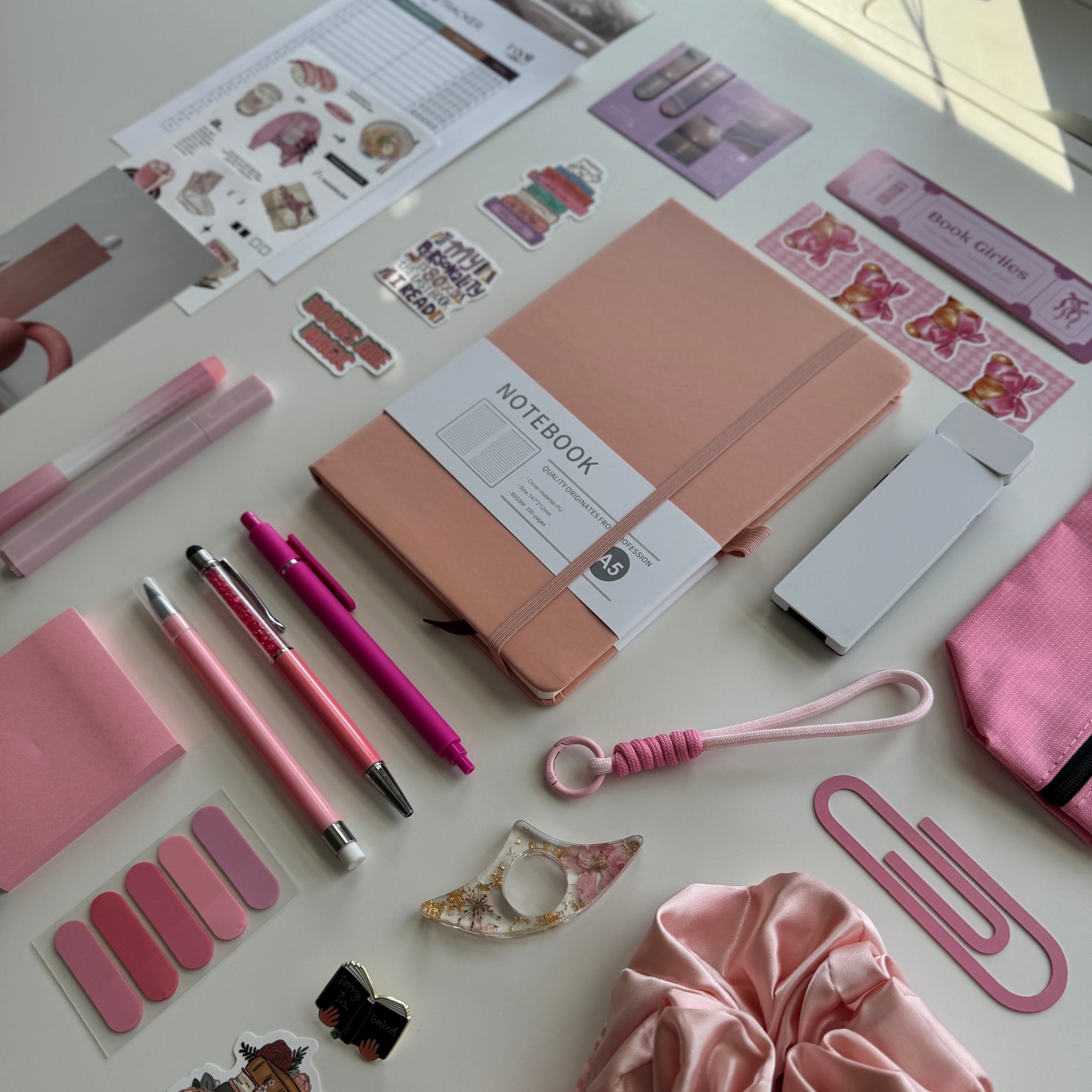 Collection of stationery items including a notebook, pens, and decorative stickers on a light surface.