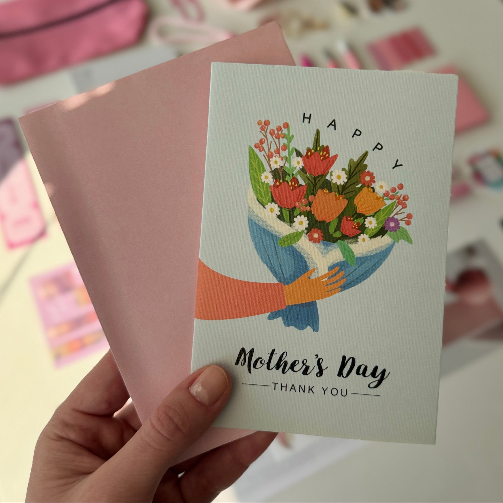 Hand holding a Mother's Day card with floral design and text.