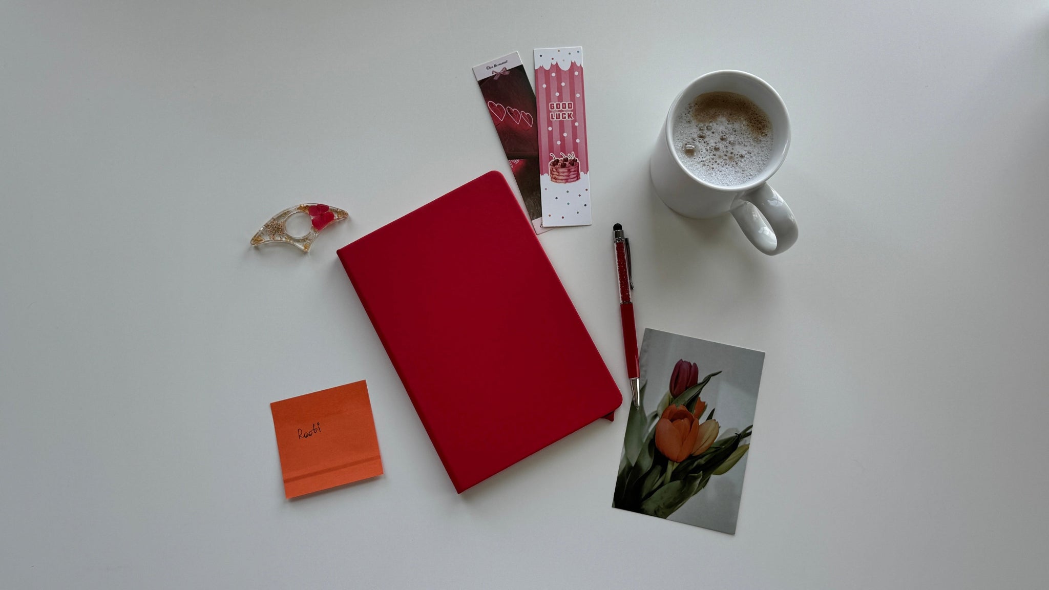 Red notebook, mug with coffee, pen, and small items on a white surface