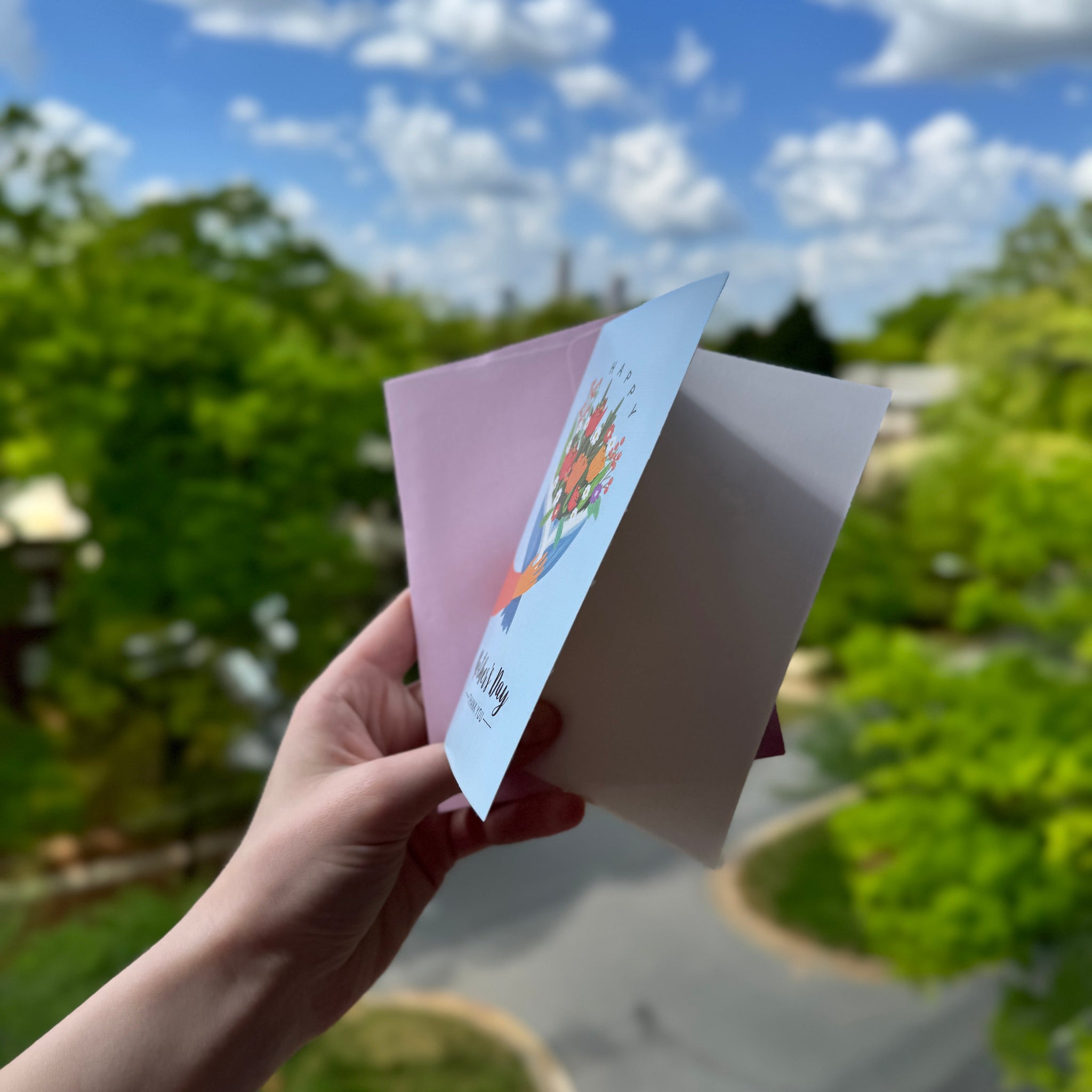 Hand holding a greeting card with a scenic background