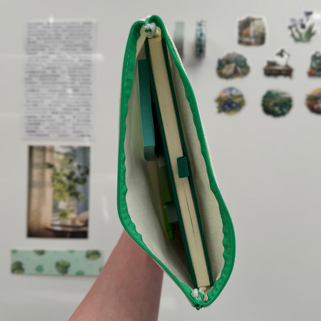 Green canvas bag held by a hand in front of a whiteboard with stickers and photos.