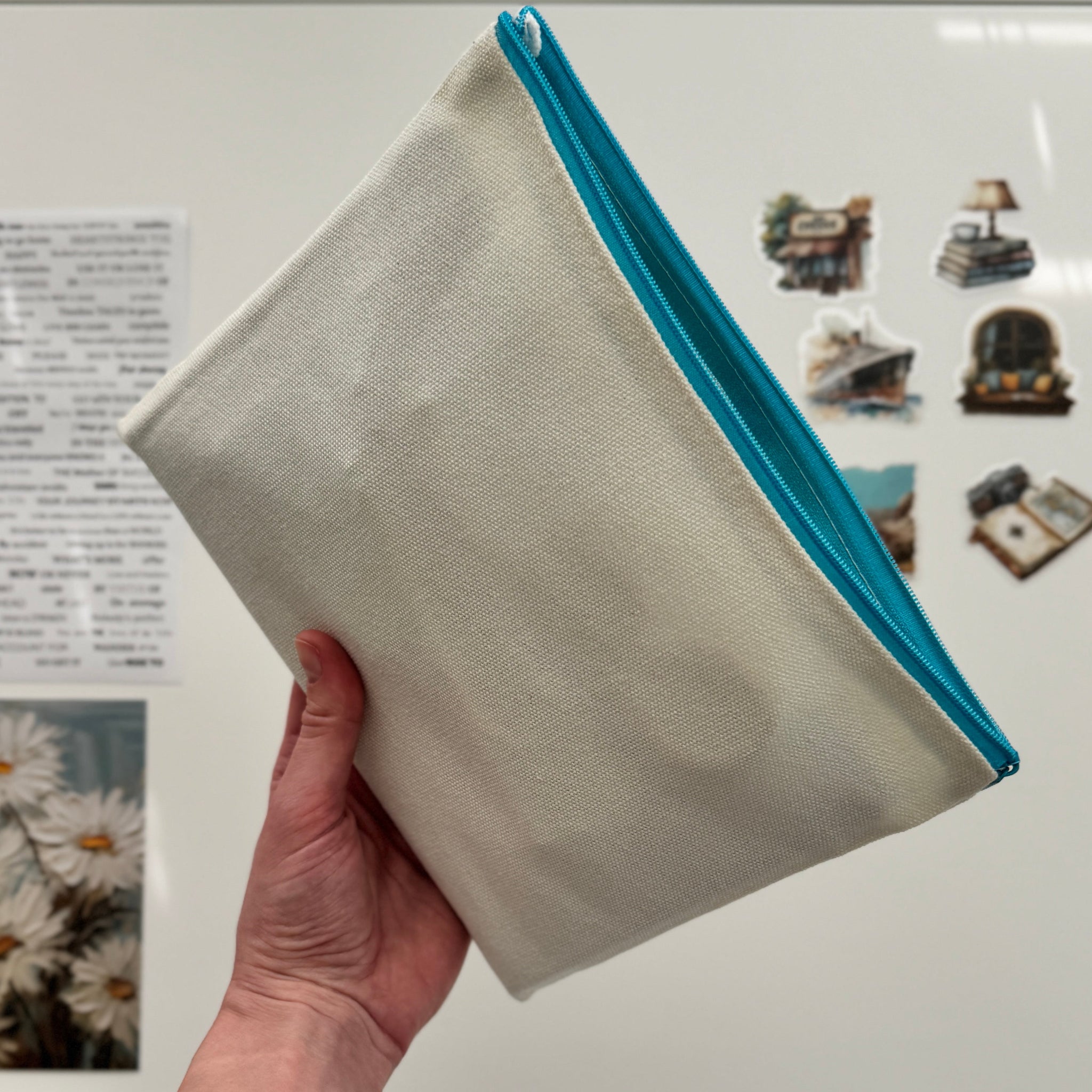 Hand holding a beige pouch with a blue zipper in front of a white appliance with stickers and photos on it.