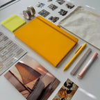 Yellow notebook, pens, and photos on a white surface