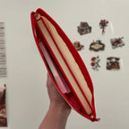 Red pouch containing pink and beige items held against a white background with decorative stickers.