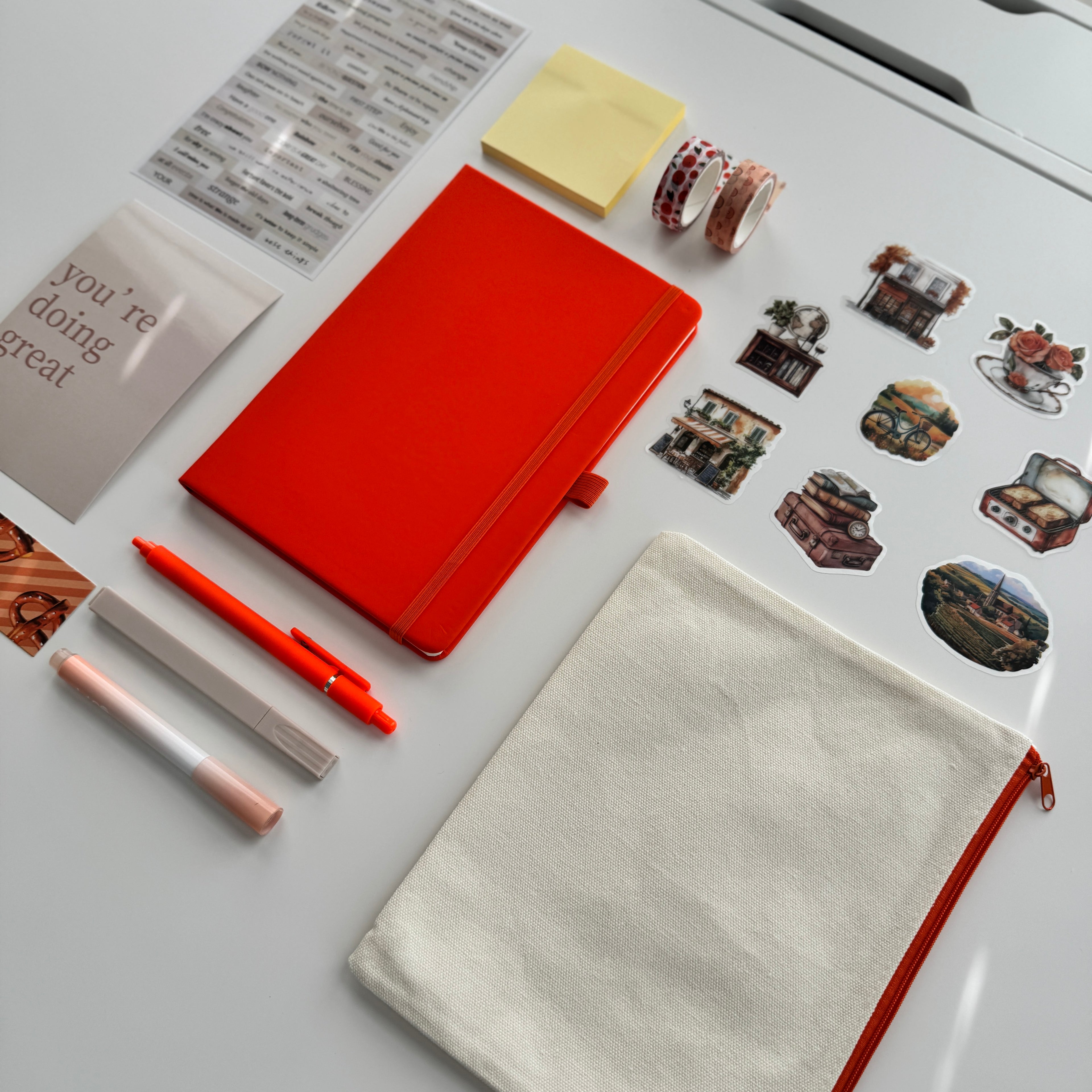 Orange notebook, pens, and stickers on a light gray surface