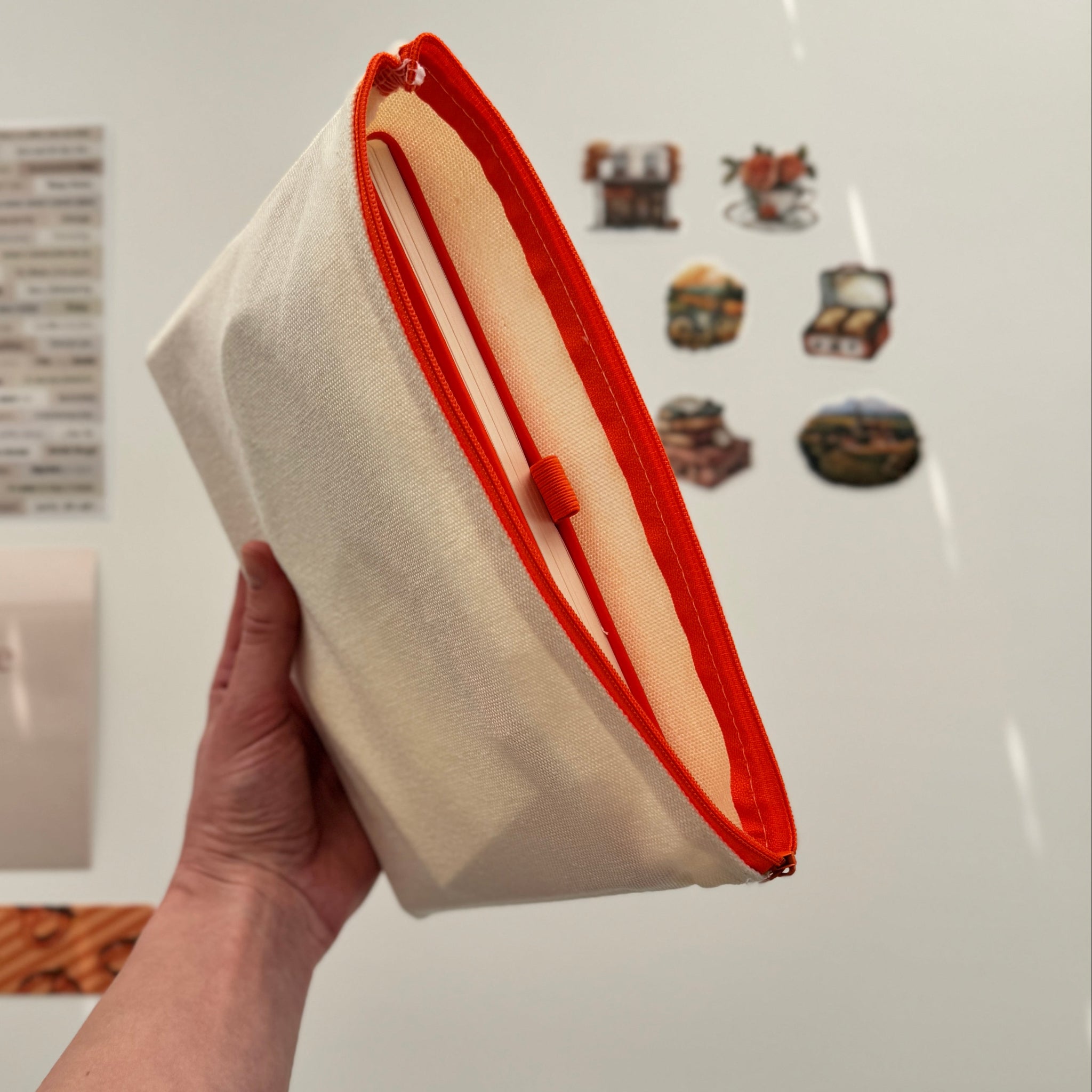 Hand holding a white pouch with red interior against a white wall with motivational posters.