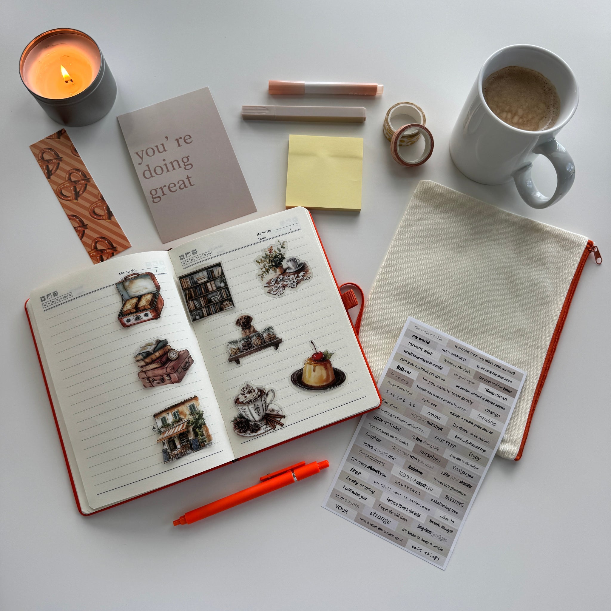 Desk with open notebook, stickers, pen, mug, and candle