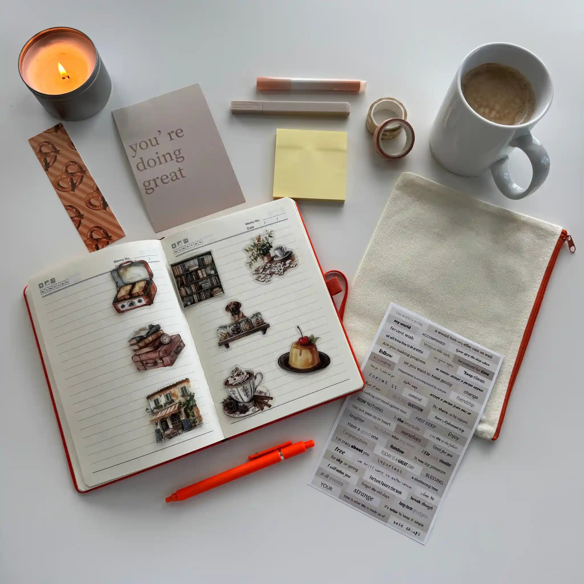 Open notebook with stickers, a mug of coffee, a candle, and stationery items on a white surface.