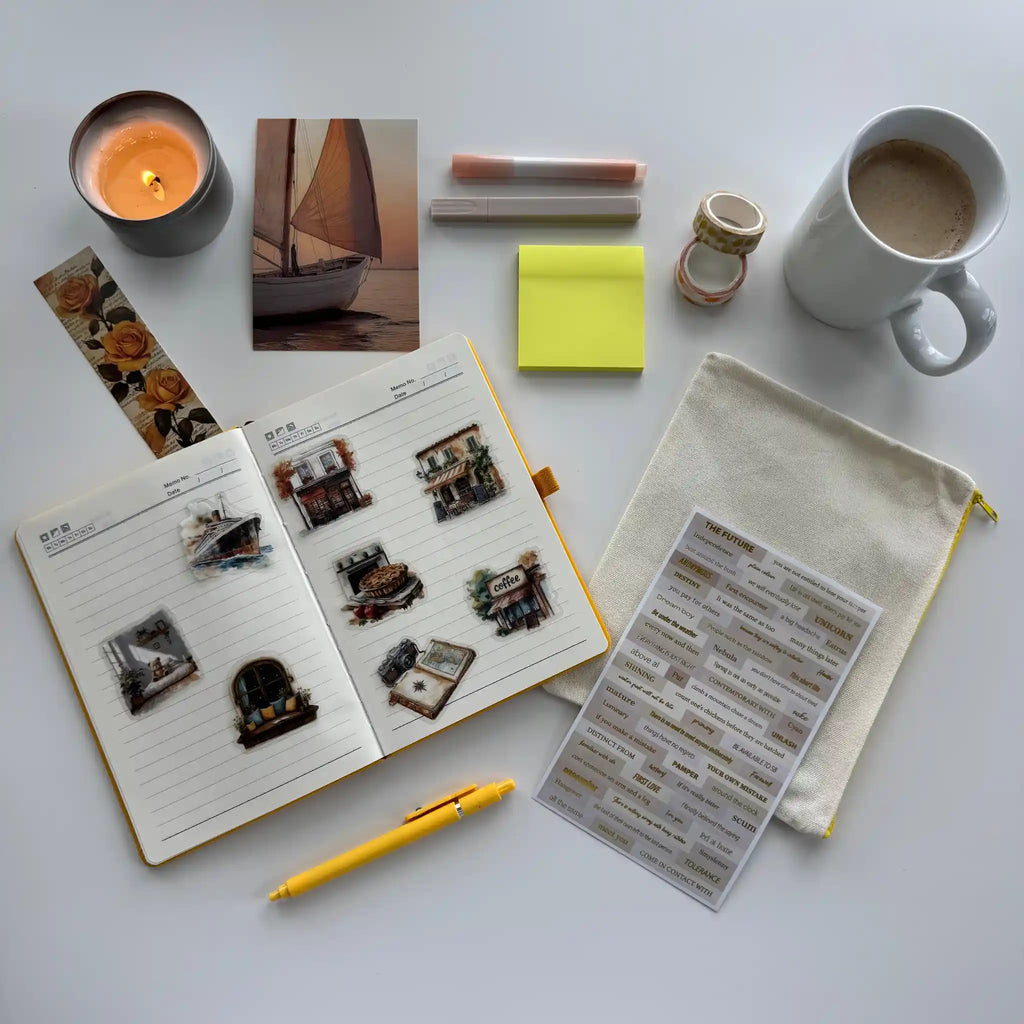 Notebook with stickers, a pen, a mug, a candle, and other items on a white surface